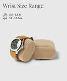 A TAWBURY Bayswater Watch Box Pillow in beige features a brown strap watch, evocative of classic designs. Another pillow rests nearby. Text on velveteen fabric indicates "Wrist Size Range 5.5–6.5 in, 14–16.5 cm," complemented by a hand icon, ensuring an elegant and comfortable display.