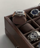 The TAWBURY Bayswater Watch Box Pillows in brown and grey elegantly showcase three watches, with one elevated on a cushion and two nestled below in plush grey velveteen compartments.