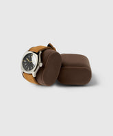 A watch with a brown leather strap rests on a Bayswater Watch Box Pillow by TAWBURY, next to a matching cushion from the same collection, all set against a light gray background.
