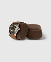 A stainless steel watch with a black dial and brown leather strap is elegantly displayed on a brown cushion beside an empty one, perfectly embodying the luxury of TAWBURY's Bayswater Watch Box Pillows in Brown/Grey, X-Small (55mm).