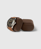 A stainless steel watch with a black dial and brown leather strap is elegantly displayed on a brown cushion beside an empty one, perfectly embodying the luxury of TAWBURY's Bayswater Watch Box Pillows in Brown/Grey, X-Small (55mm).