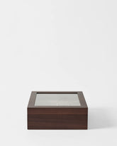 The TAWBURY Grove 12 Slot Wooden Watch Box in dark walnut wood features a glass lid and is shown on a plain white background, making it a stylish display case for your watches.