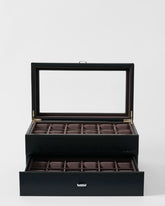 The TAWBURY Bayswater 24 Slot Watch Box with Drawer in Black/Charcoal features a glass lid for display, two tiers of brown fabric-lined compartments—one visible and one drawer—ideal for storing and showcasing your watches elegantly.