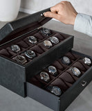 A person opens the TAWBURY Bayswater 24 Slot Watch Box with Drawer in Black/Charcoal, revealing luxury watches organized in two rows within individual PU leather compartments and a charcoal interior.