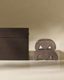A TAWBURY Grove Watch Pillow in brown sits beside a large brown hair claw clip on a beige surface with a neutral background.