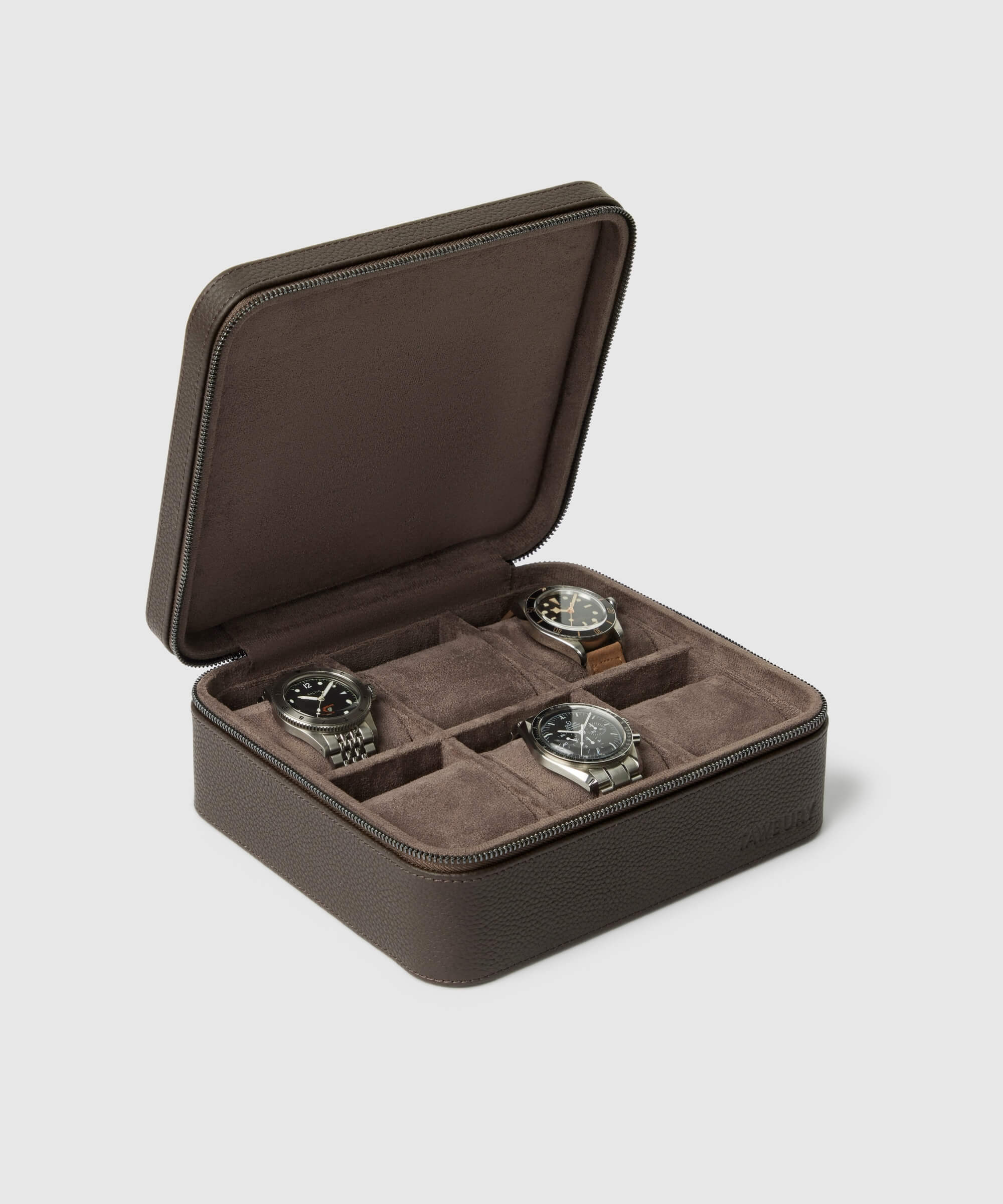 Against a gray background, the TAWBURY Fraser 6 Watch Case in brown elegantly displays four compartments, showcasing three exquisite timepieces.
