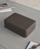 From the TAWBURY Fraser Collection, the Fraser 8 Watch Case in brown leather features rounded edges and sits elegantly on a light gray surface, surrounded by open magazinesâideal for watch collectors seeking a stylish and organized case.