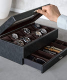 A person opens a TAWBURY Bayswater 12 Slot Watch Box in Black/Charcoal, crafted from PU leather, unveiling eight watches in its scratch-free interior with a drawer below for sunglasses and watch straps.