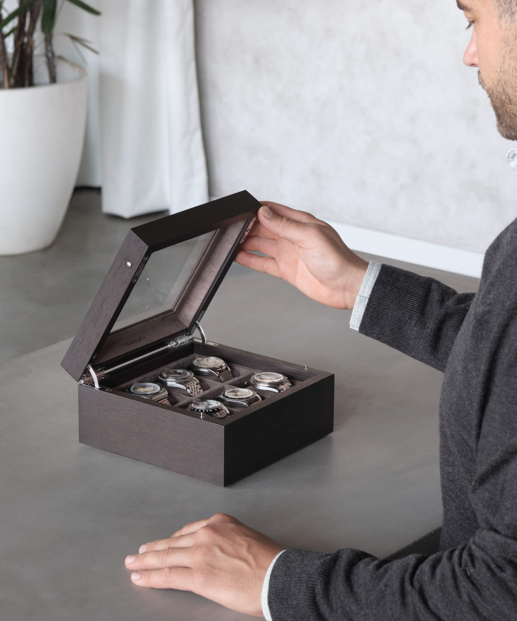 A man is opening a TAWBURY Grove 6 Slot Watch Box with Glass Lid to display his timepieces on a table.