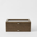 The TAWBURY Bayswater 12 Slot Watch Box with Storage in Driftwood Taupe features a closed glass top and two silver handles, displayed against a plain white background.