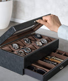 A person opens the TAWBURY Bayswater 12 Slot Watch Box with Storage in black/grey, unveiling eight exquisite watches and compartments filled with collector essentials and stylish sunglasses.