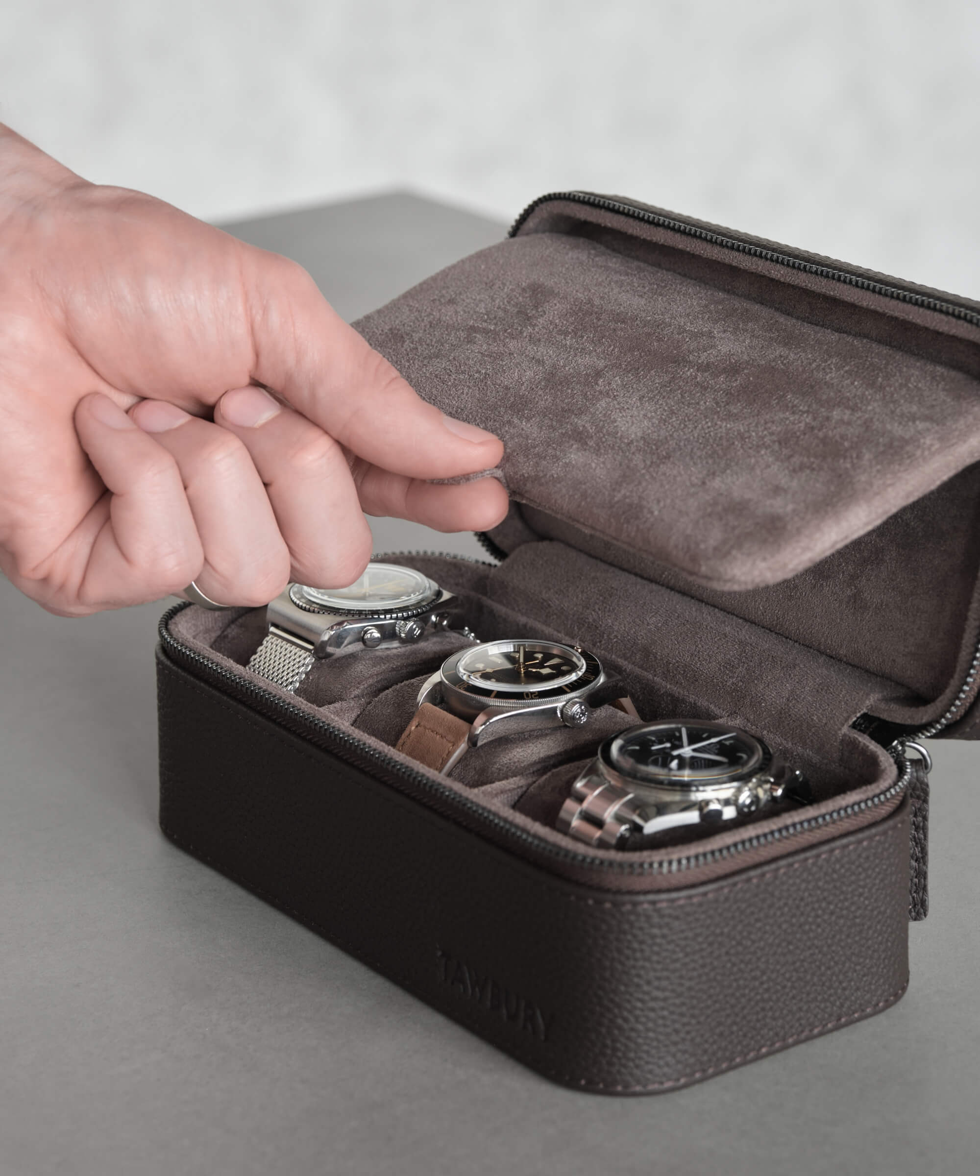 The TAWBURY Fraser 3 Watch Travel Case - Brown offers a sleek black travel case made from genuine leather. It features red stitching accents and a convenient carrying handle. The case includes a watch cushion that securely holds up to three timepieces.