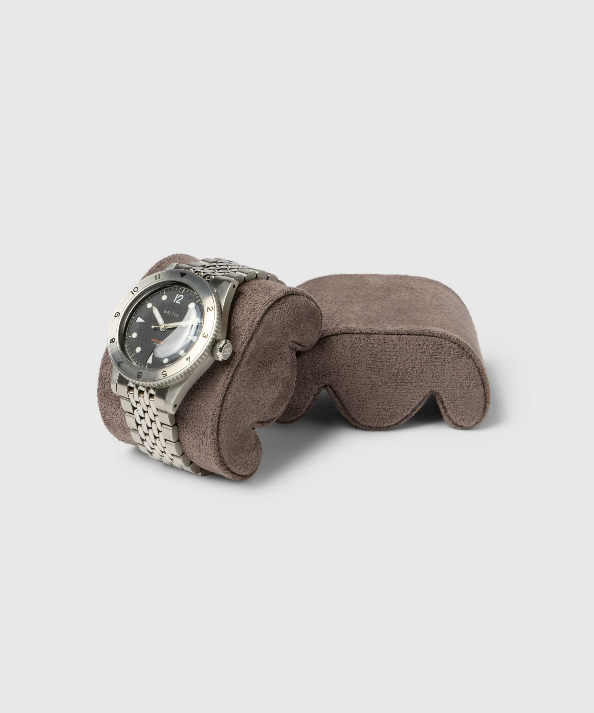 A silver wristwatch with a black dial and metal strap is elegantly showcased on a gray cushion, ideal for slender wrists. Perfectly placed in a TAWBURY Grove Watch Box Pillows - X-Small - Brown, it complements any collector's display against the light gray background.