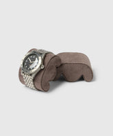 A silver wristwatch with a black dial and metal strap is elegantly showcased on a gray cushion, ideal for slender wrists. Perfectly placed in a TAWBURY Grove Watch Box Pillows - X-Small - Brown, it complements any collector's display against the light gray background.