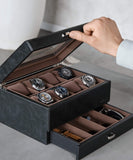 A watch enthusiast opens the TAWBURY Bayswater 8 Slot Watch Box in black/grey vegan leather, revealing six exquisite wristwatches and additional storage beneath.