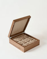 The TAWBURY Grove 12 Slot Wooden Watch Box in Light Walnut features a solid lid and multiple beige cushioned slots for storing watches or accessories, all with classic elegance.
