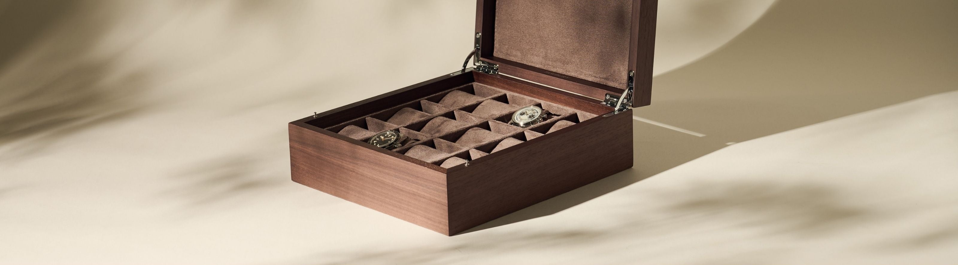 A wooden watch box with an open lid displays three watches inside, resting in separate compartments lined with brown fabric.