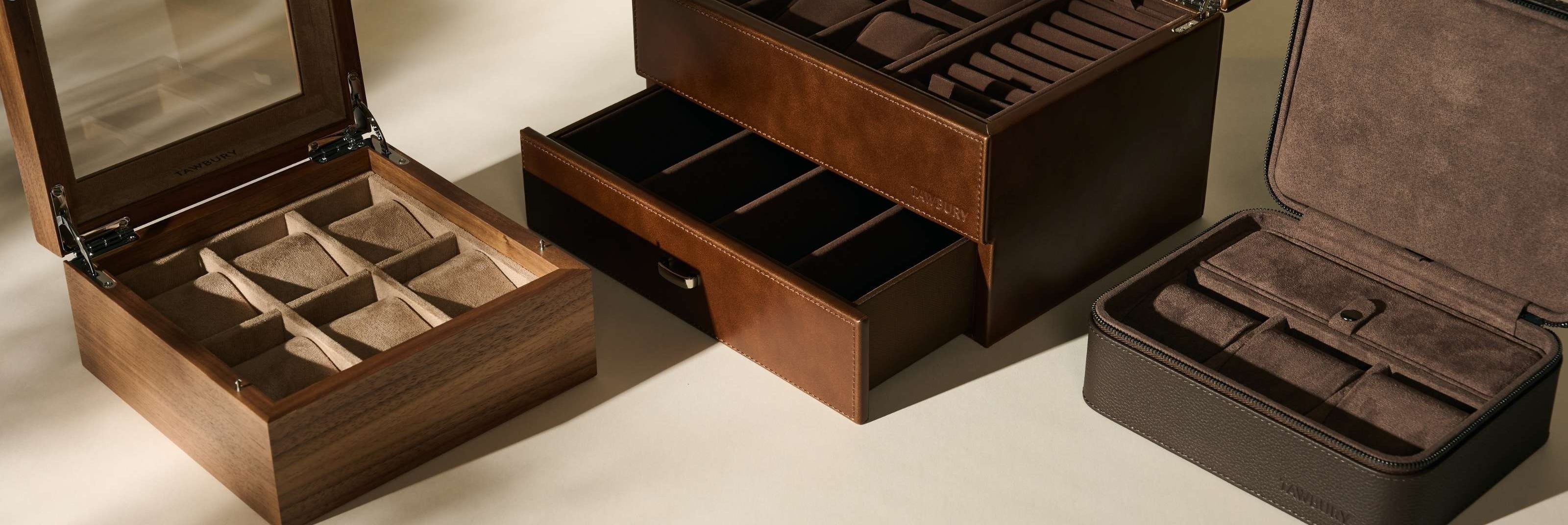 Three different jewelry and watch storage boxes, each open to display divided compartments lined with soft fabric, arranged on a neutral surface.