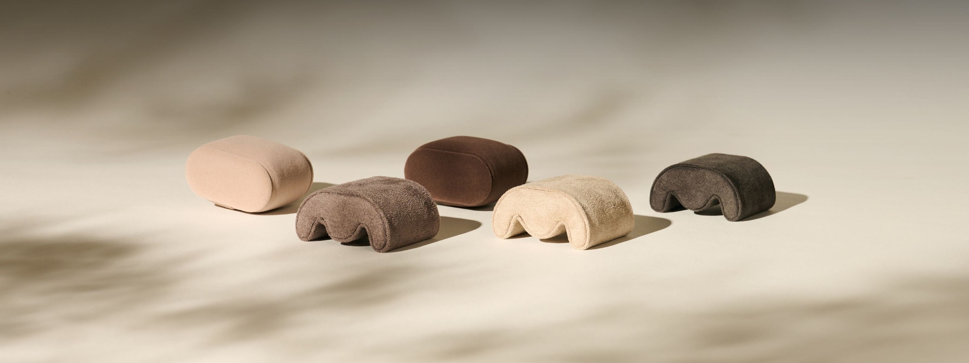Five small, rounded, legged stools in various neutral tones are arranged on a light surface.