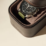 A black chronograph watch with a green strap is kept inside the TAWBURY Fraser 1 Watch Case - Brown, which features textured leather and a soft fabric lining.