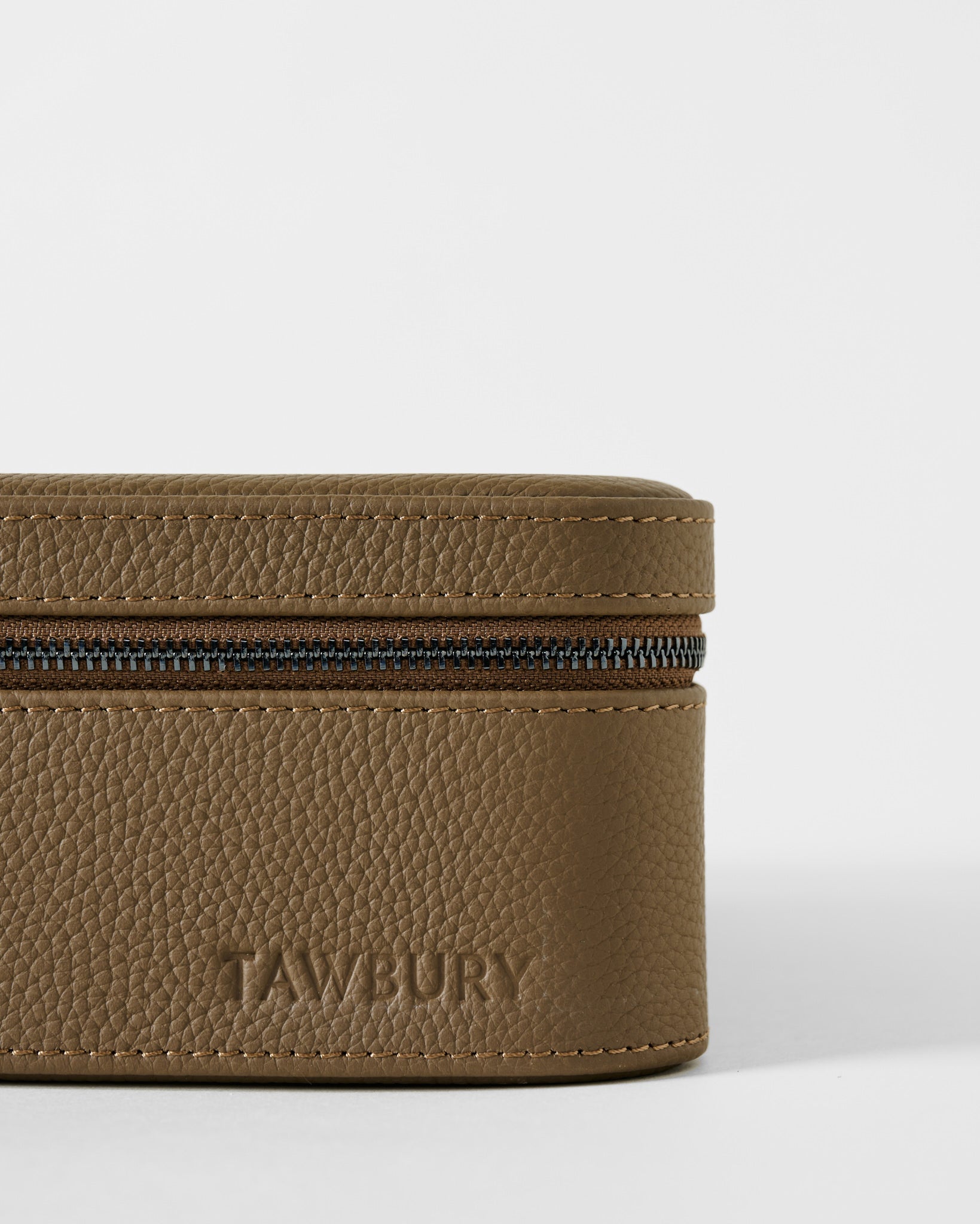 Close-up of a TAWBURY Fraser 3 Watch Case with Storage - Truffle Taupe, featuring a taupe leather exterior with a zippered closure and an embossed logo on the side.