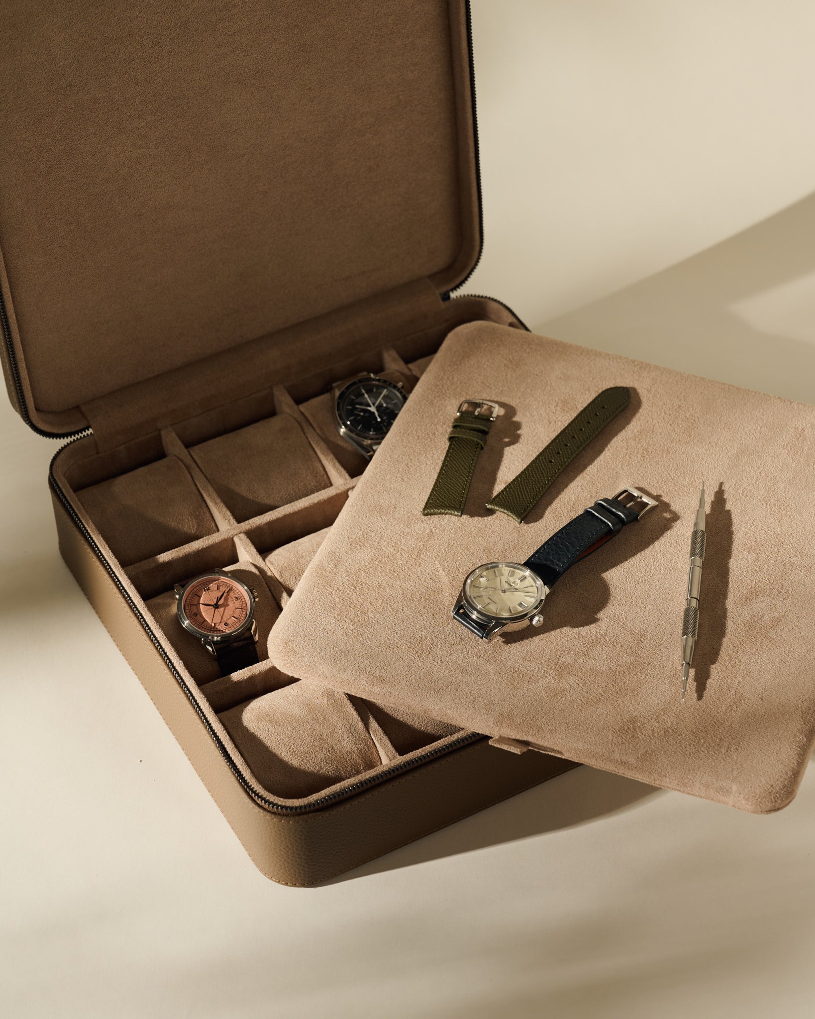 An open TAWBURY Fraser 12 Watch Case in Truffle Taupe containing two wristwatches, with a tray holding an additional watch, two watch straps, and a spring bar tool.