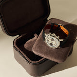 An open TAWBURY Fraser 2 Watch Case - Espresso Brown with a cushioned insert holding a silver chronograph wristwatch with a black leather strap.