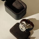 An open black leather TAWBURY Fraser 1 Watch Case - Midnight Black sits next to a wristwatch resting on a removable interior cushion.