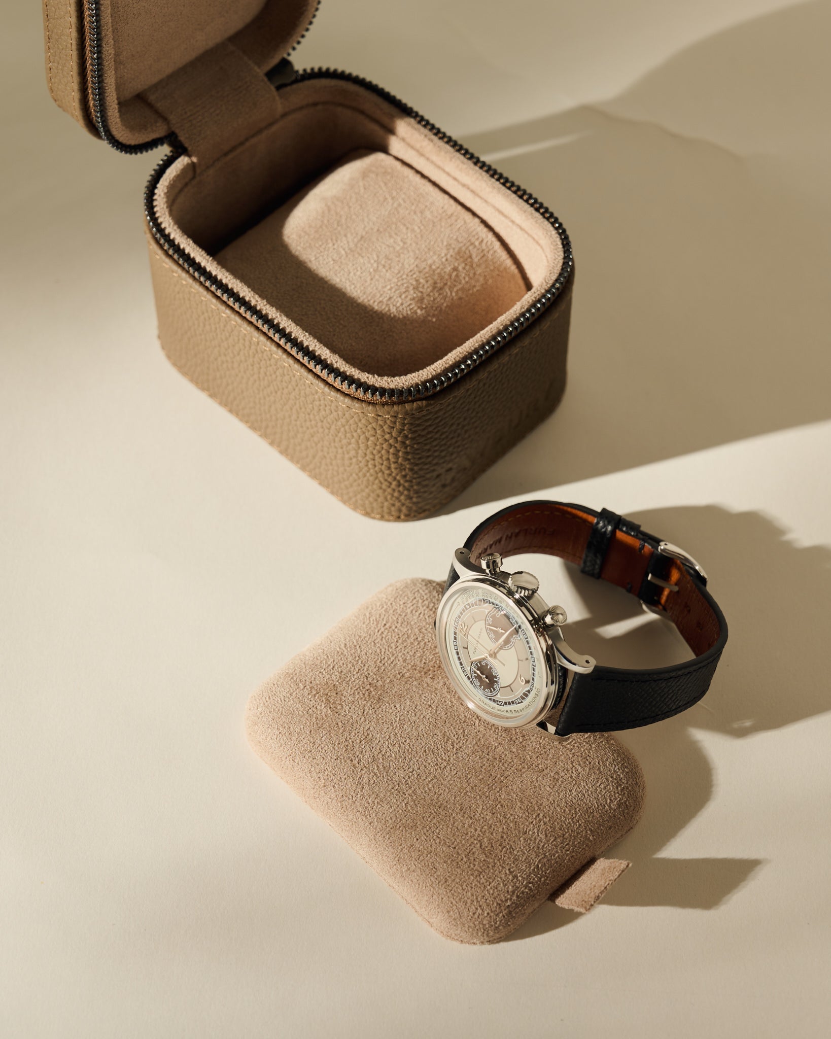 An open TAWBURY Fraser 1 Watch Case - Truffle Taupe with its removable cushion sitting in front, holding a silver wristwatch with a black leather strap.