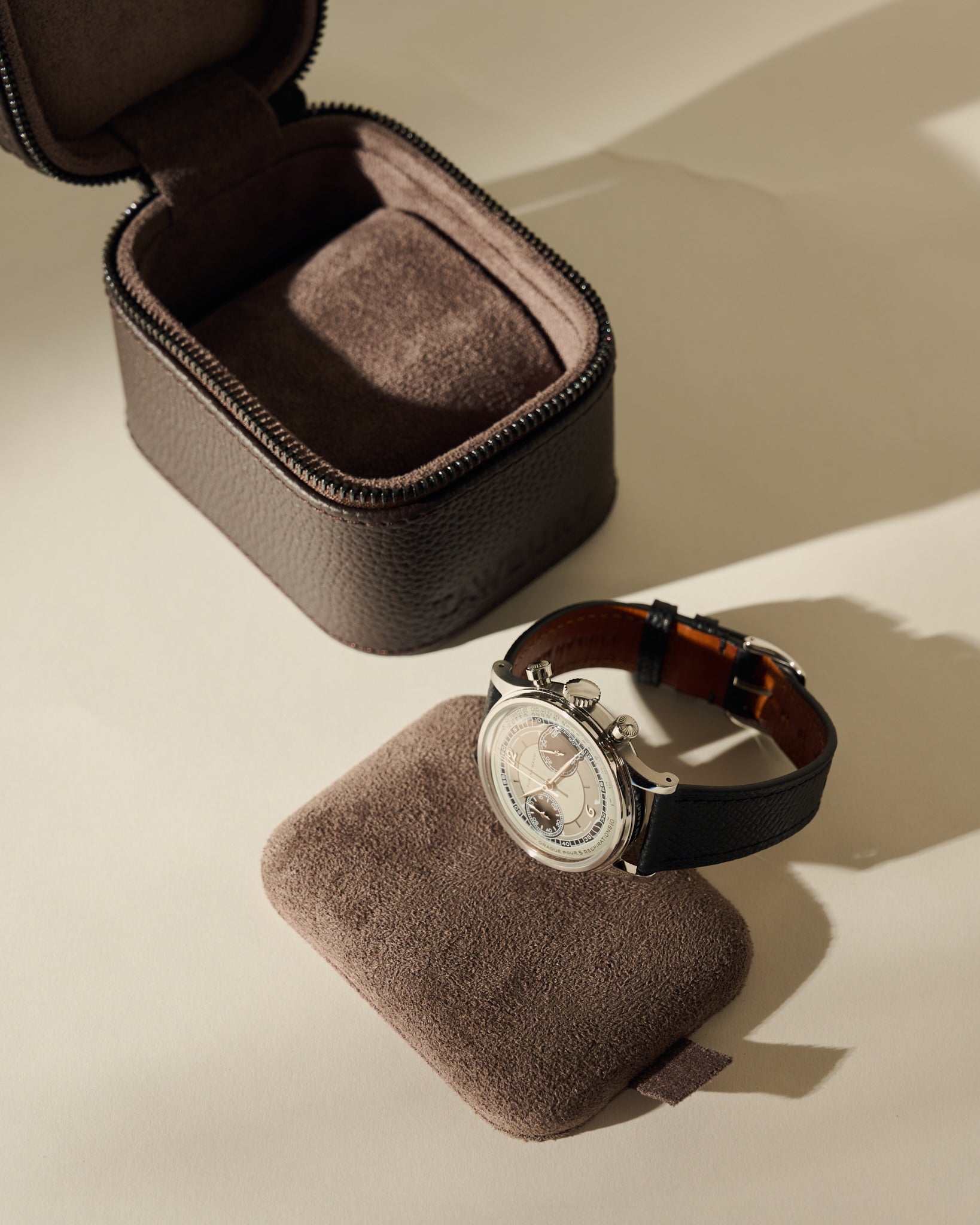 An open, dark brown Fraser 1 Watch Case - Espresso Brown sits behind a luxury wristwatch resting on a matching brown cushion.