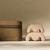 The TAWBURY Fraser 4 Watch Case in Truffle Taupe, with its textured brown leather finish, sits beside two curvy beige suede forms on a neutral background—perfect for stylish watch storage or travel.