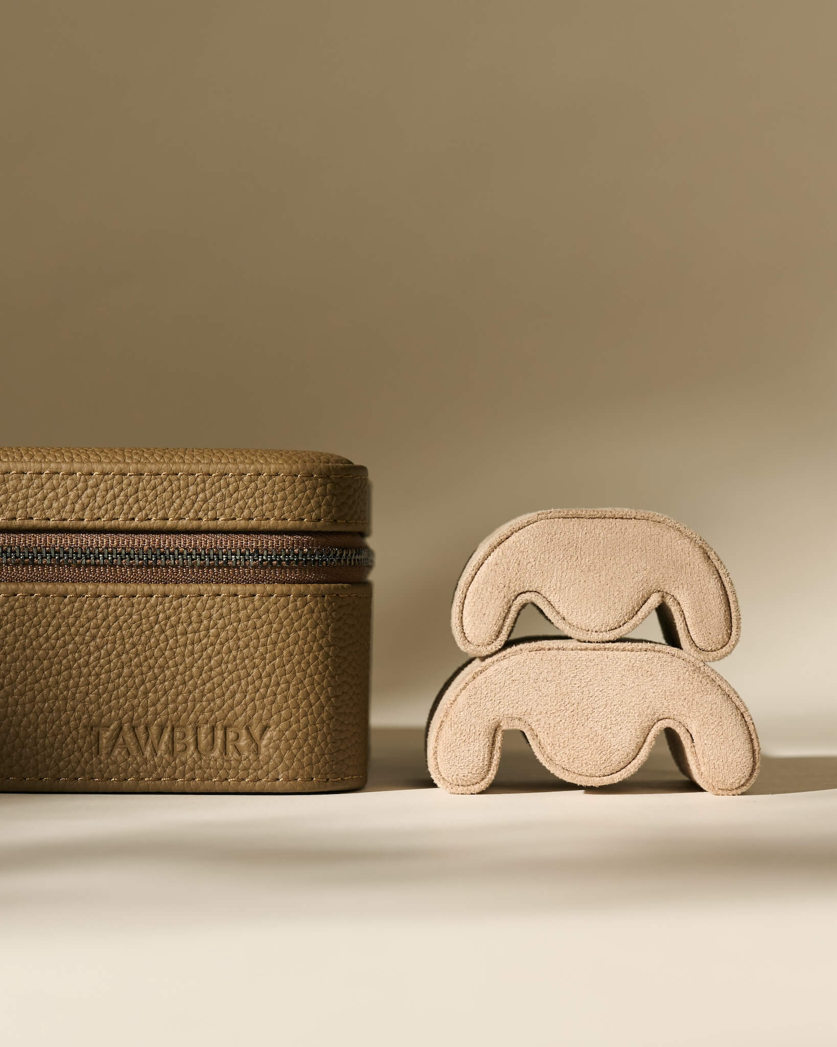 A taupe textured leather TAWBURY Fraser 3 Watch Case - Truffle Taupe next to two stacked watch pillows.