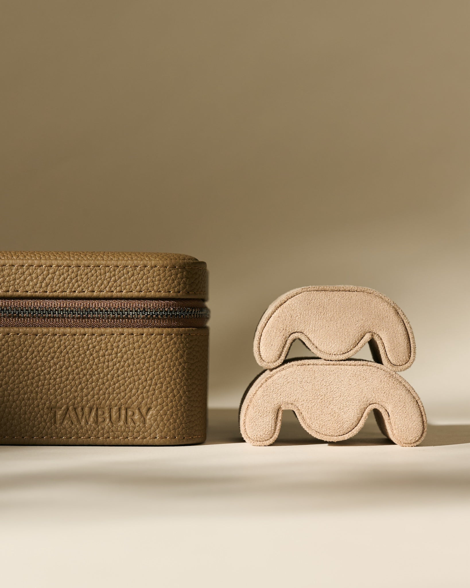 The TAWBURY Fraser 3 Watch Case with Storage in Truffle Taupe sits beside two stacked beige suede watch cushions against a neutral background.