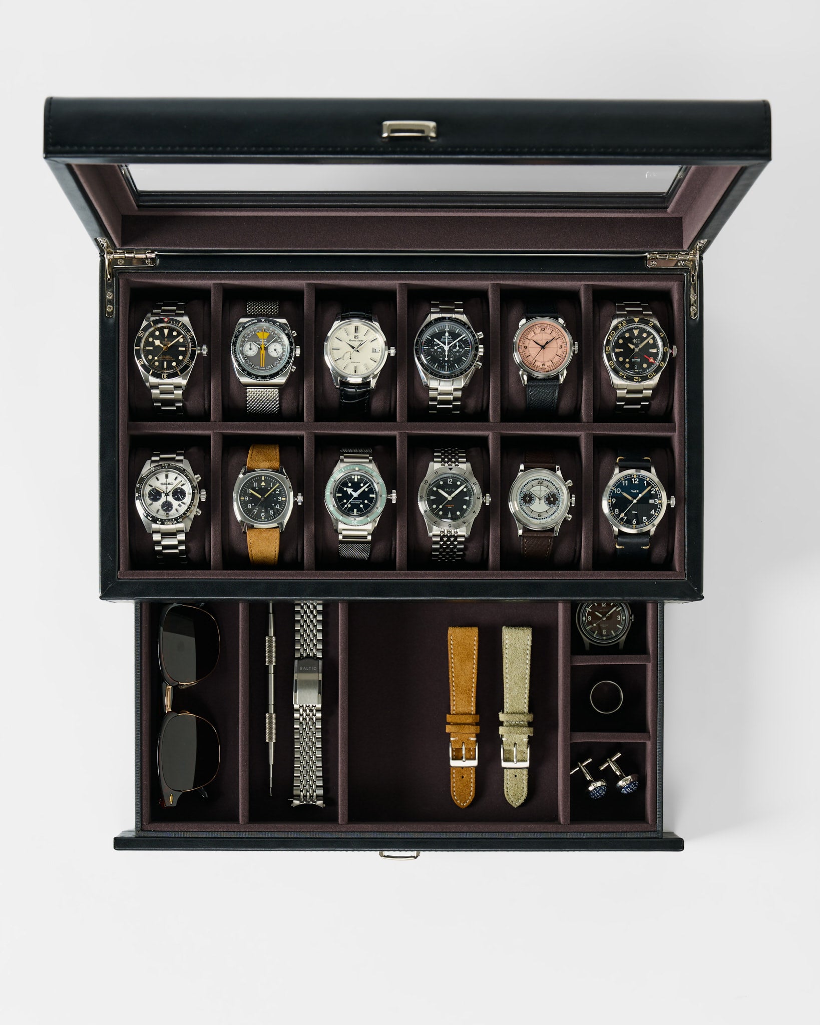 The TAWBURY Bayswater 12 Slot Watch Box with Storage in Black/Charcoal neatly displays twelve wristwatches, sunglasses, watch straps, a watch tool, cufflinks, and a tie clip under a glass lid.