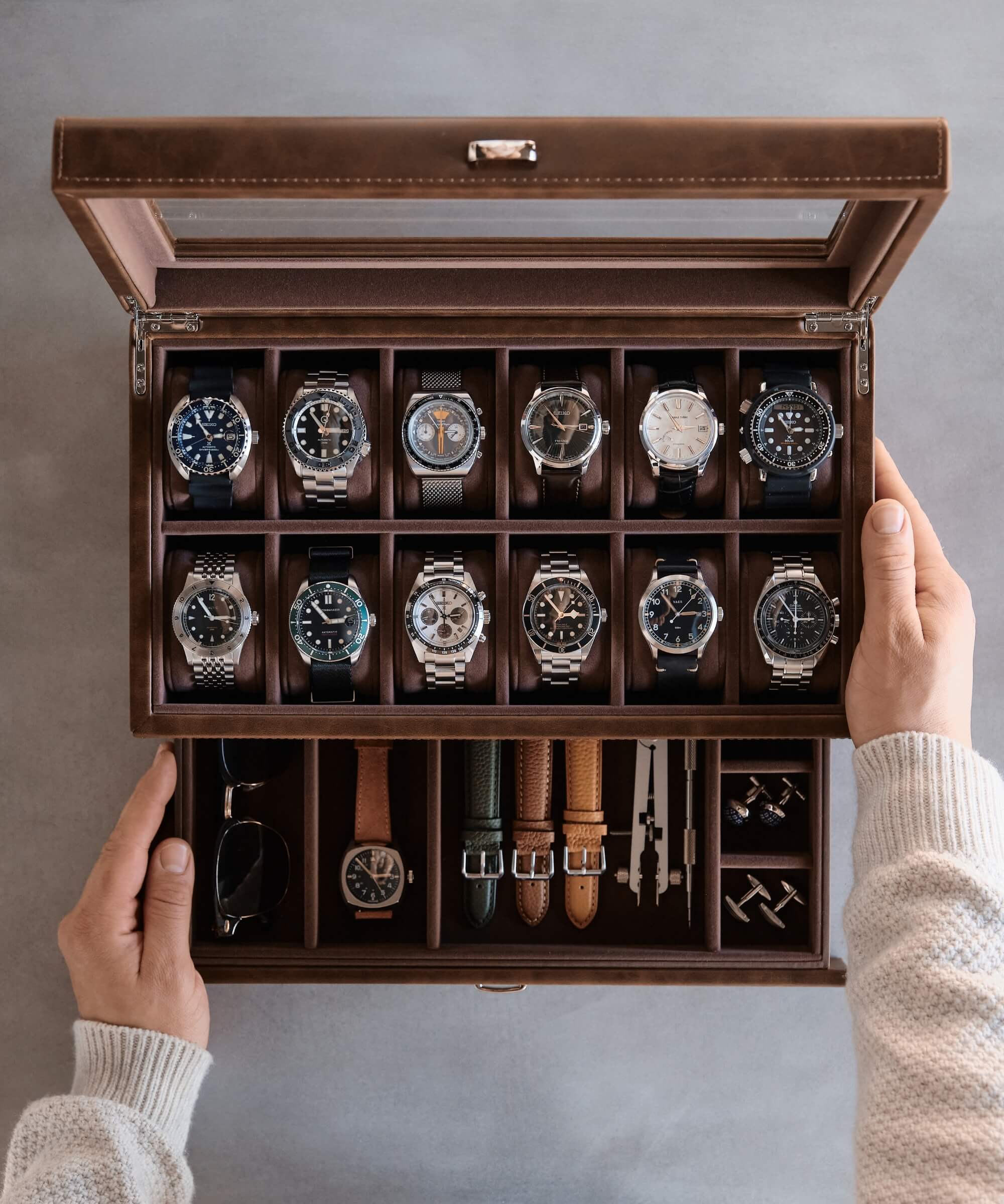 A person holding a TAWBURY Bayswater 12 Slot Watch Box with Drawer - Brown filled with timepieces.