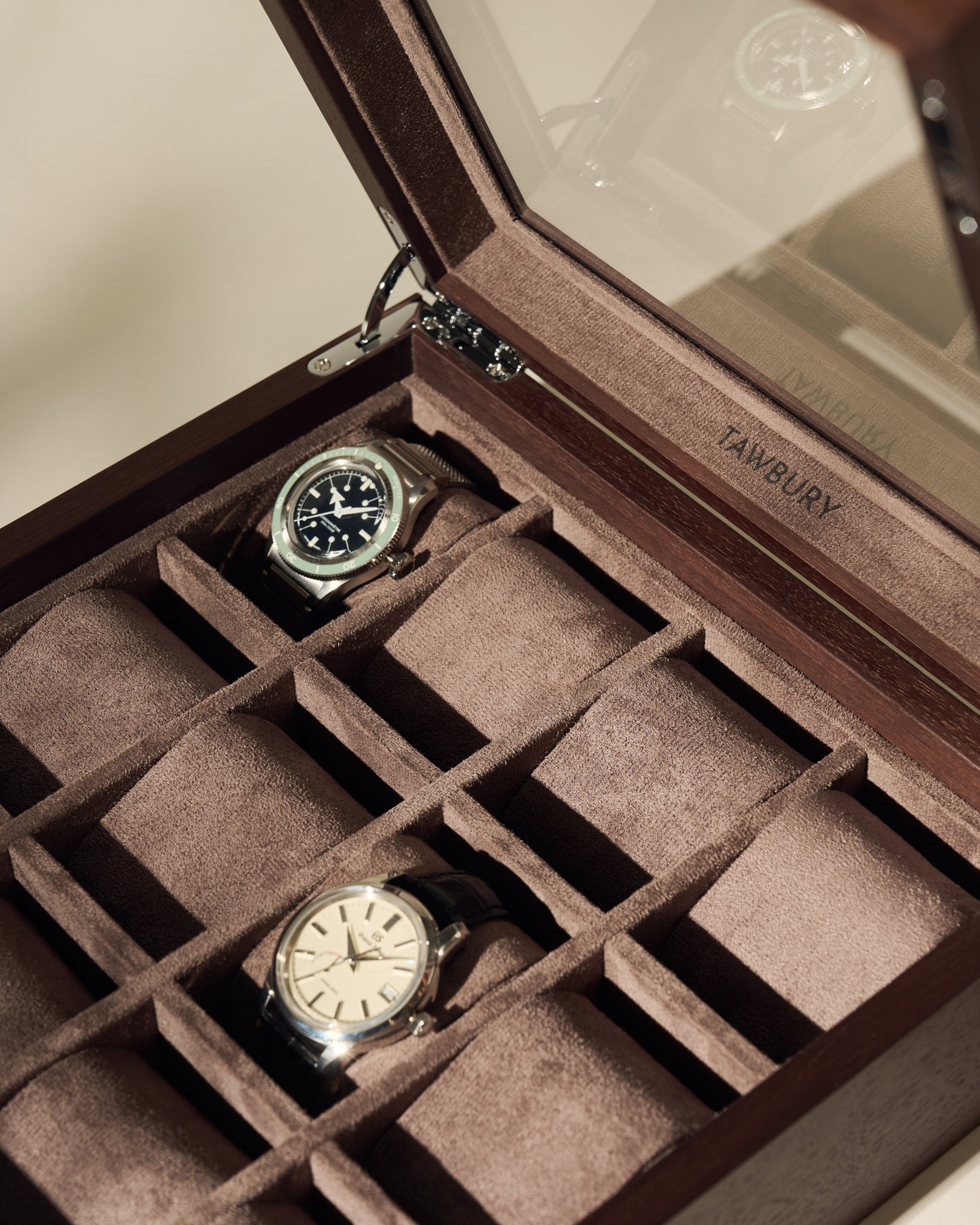 The TAWBURY Grove 12 Slot Wooden Watch Box in dark walnut wood features a glass lid, individual compartments, and brown suede lining—perfect for collectors to stylishly display and protect their wristwatches.
