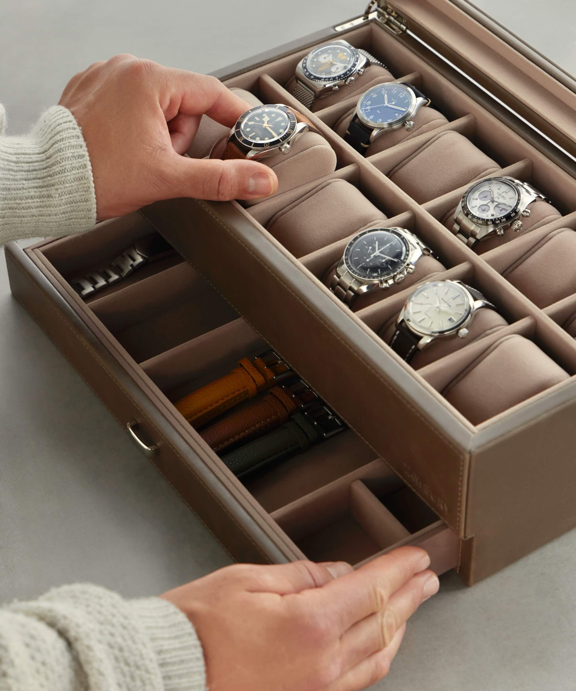 As the taupe Bayswater 12 Slot Watch Box from TAWBURY is opened, it unveils a breathtaking assortment of eight wristwatches, making it an ideal choice for any watch collector, with extra straps thoughtfully stored inside.