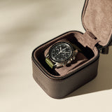 The TAWBURY Fraser 1 Watch Case in brown displays a wristwatch with a black dial and green strap, offering stylish travel storage on a neutral background.