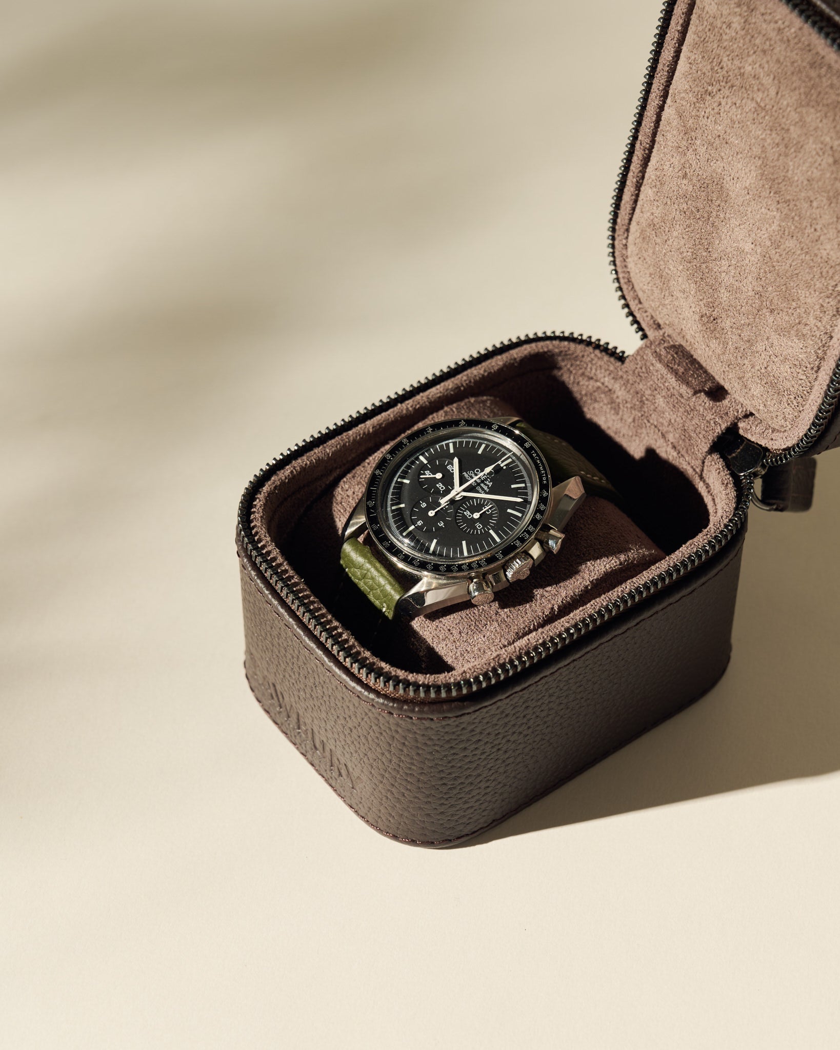 The TAWBURY Fraser 1 Watch Case in brown displays a wristwatch with a black dial and green strap, offering stylish travel storage on a neutral background.