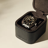 A black and silver wristwatch with a black dial is displayed in an open TAWBURY Fraser 1 Watch Case - Black on a light surface.