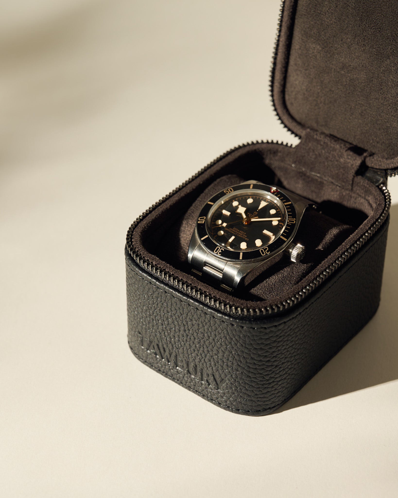 A black and silver wristwatch with a black dial is displayed in an open TAWBURY Fraser 1 Watch Case - Black on a light surface.