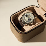 A wristwatch with a brown leather strap and silver casing is displayed inside the TAWBURY Fraser 1 Watch Case - Taupe, featuring a soft suede interior.