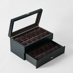 The TAWBURY Bayswater 24 Slot Watch Box with Drawer in Midnight Black features multiple compartments, a glass lid for display, and a lower pull-out drawer, all lined with dark brown fabric—ideal for organized watch storage.
