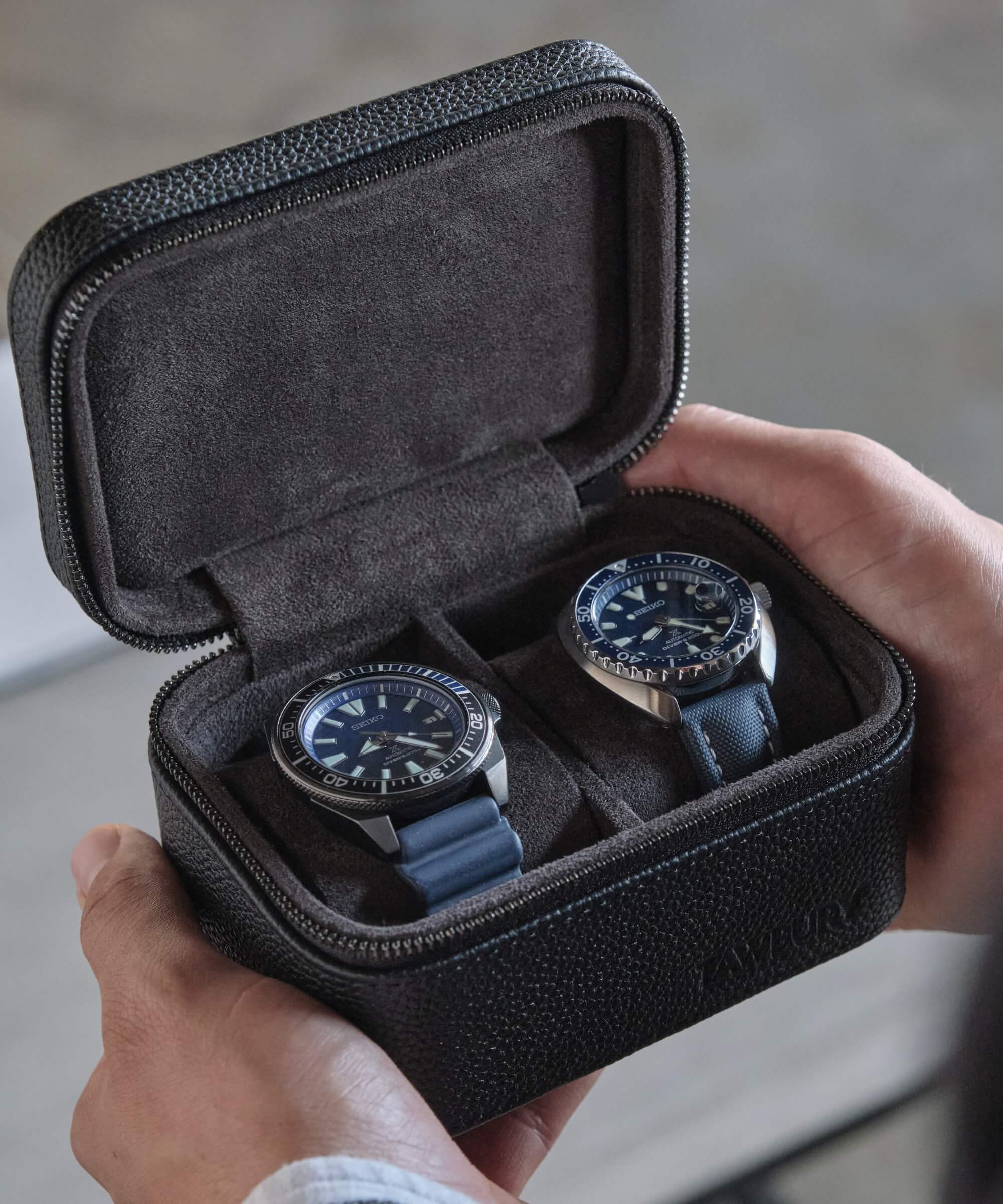 A person holding two watches in a TAWBURY Fraser 2 Watch Travel Case - Black, protecting their valuable timepieces.