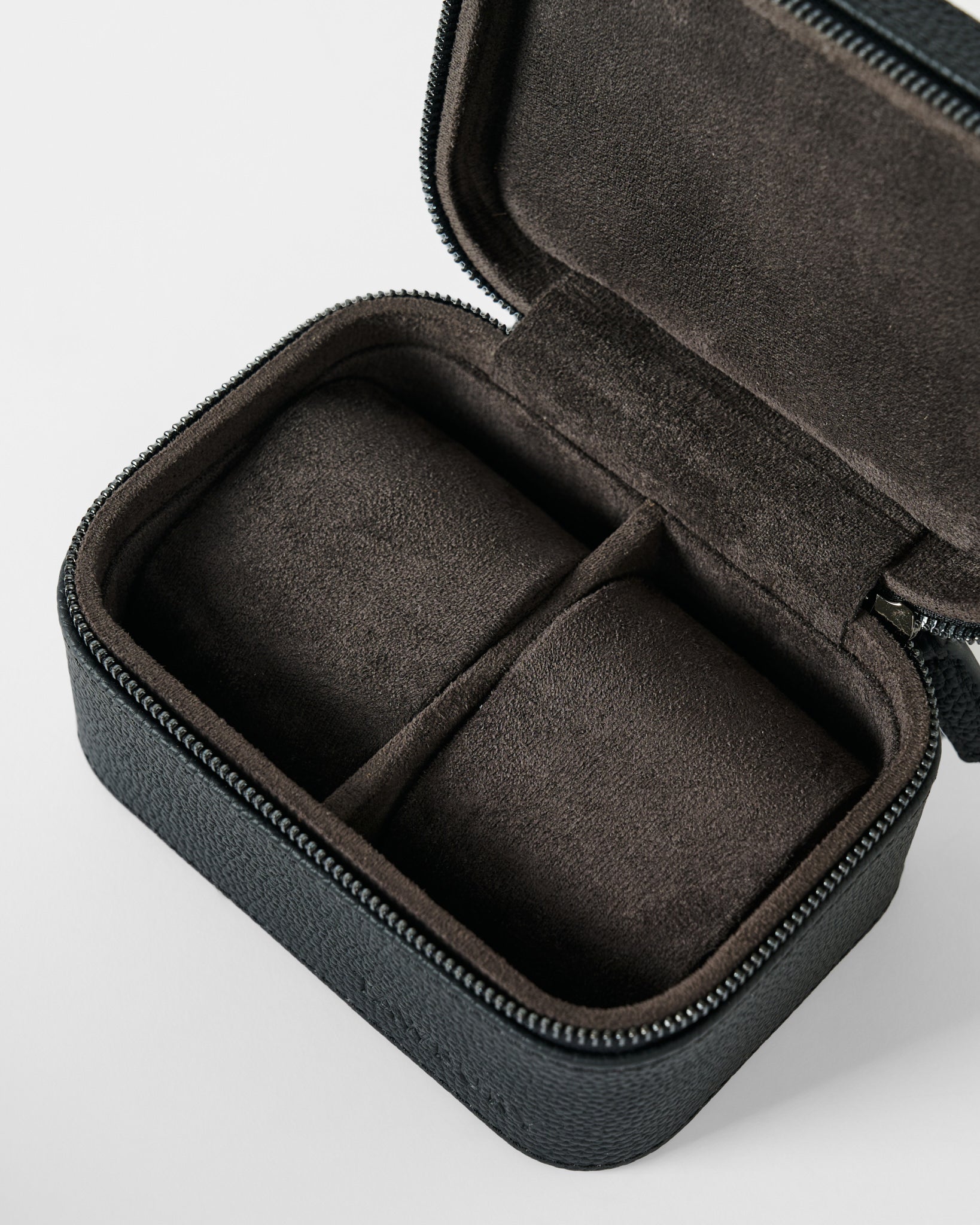 The TAWBURY Fraser 2 Watch Case - Black is a compact, rectangular leather travel case with a black zip exterior and soft brown divided interior, designed to securely store and protect two watches or jewelry on the go.