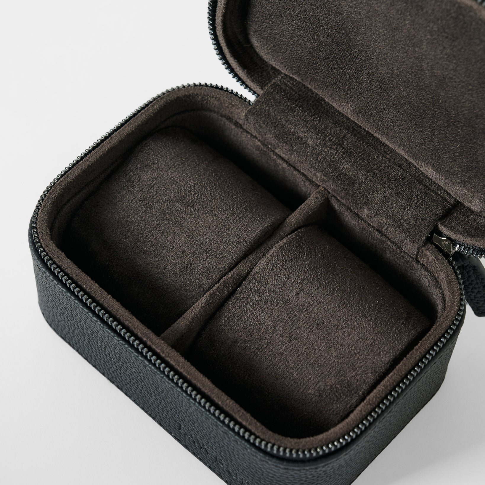 The TAWBURY Fraser 2 Watch Case - Black is a compact, rectangular leather travel case with a black zip exterior and soft brown divided interior, designed to securely store and protect two watches or jewelry on the go.