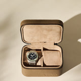 A silver wristwatch with a black face is placed inside the TAWBURY Fraser 2 Watch Case in taupe, a brown leather case featuring suede lining and two compartments.