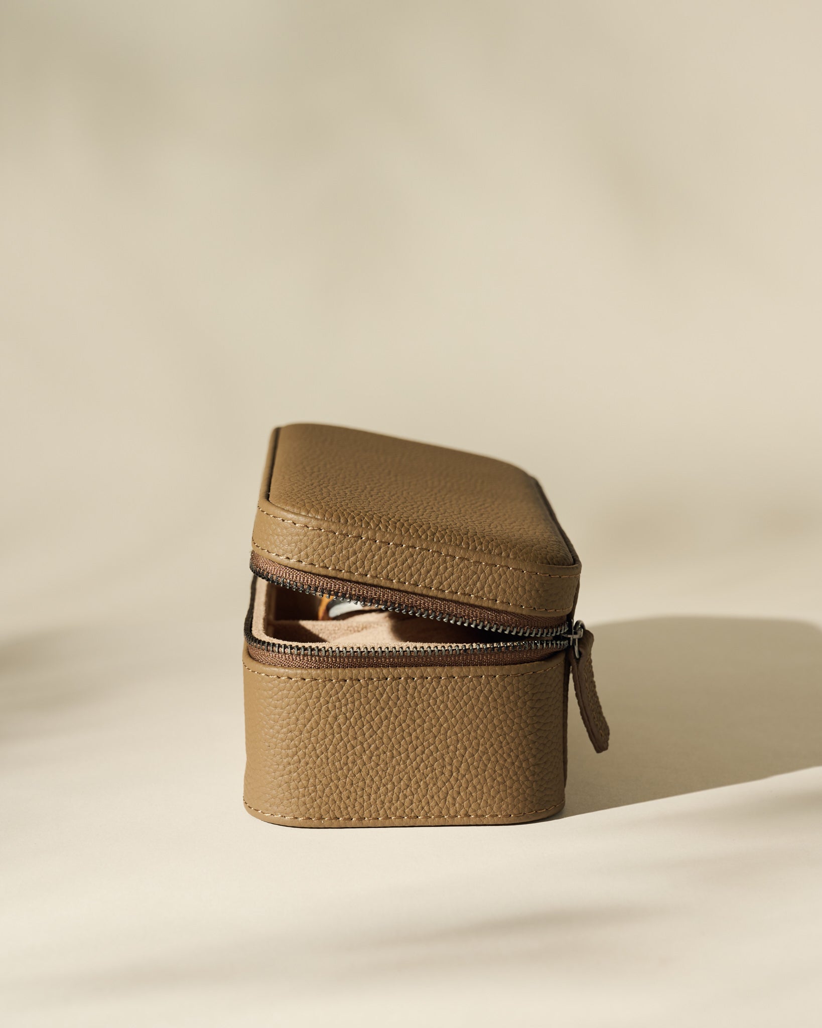 The TAWBURY Fraser 3 Watch Case in taupe textured leather, featuring a zippered closure, rests partially open on a softly lit, neutral background.