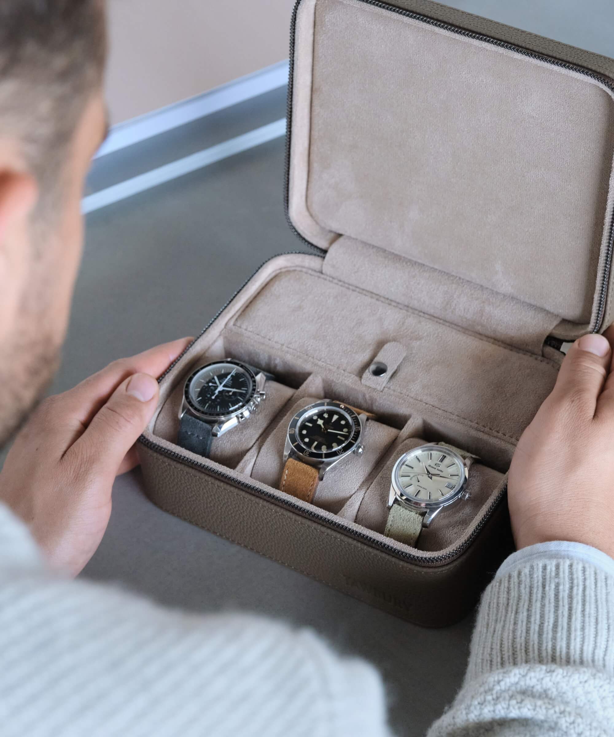 A man is holding three TAWBURY Fraser 3 Watch Travel Cases with Storage - Taupe.