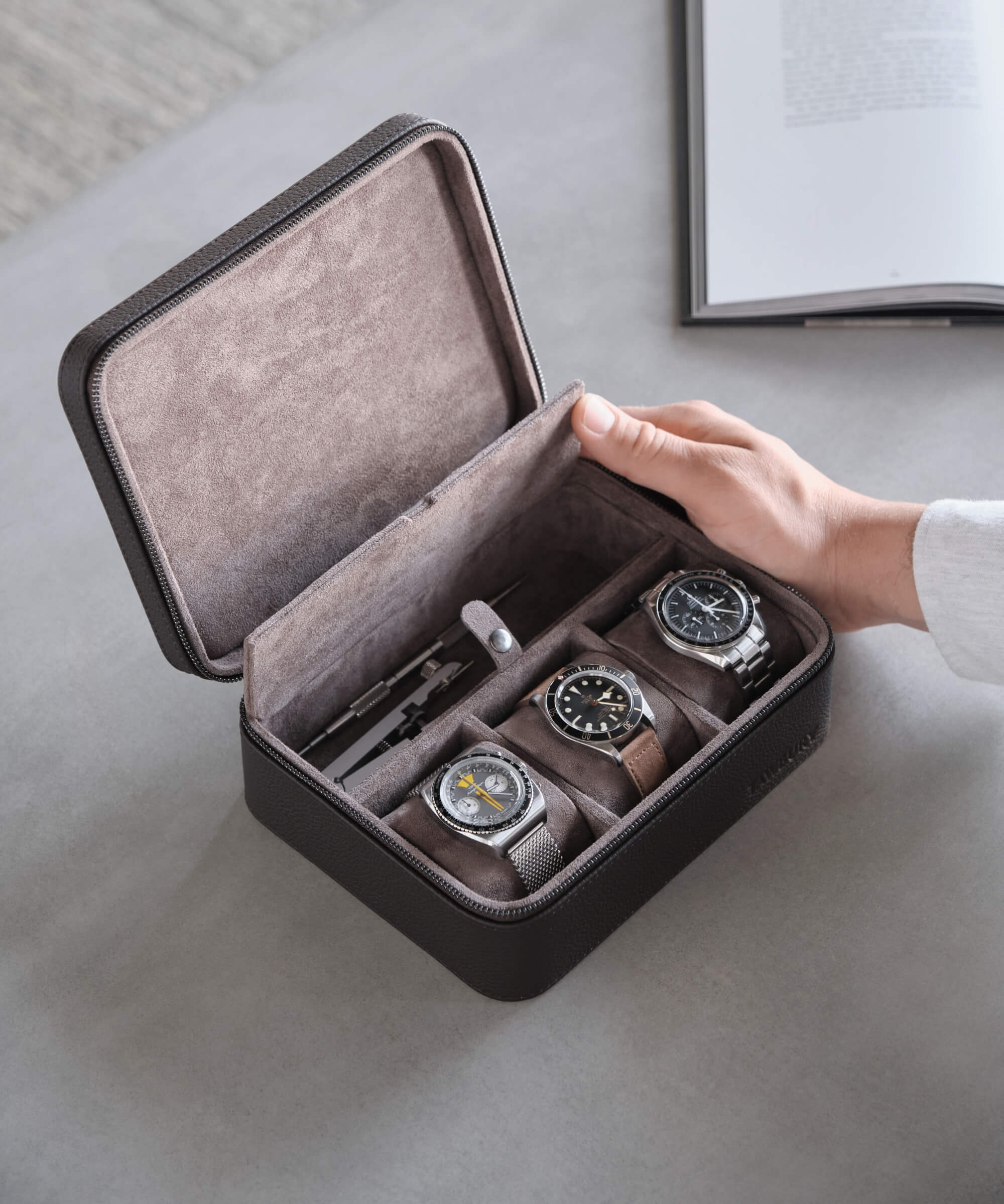 A person demonstrating the functionality of a TAWBURY Fraser 3 Watch Travel Case with Storage - Brown by holding a watch securely inside an open box.